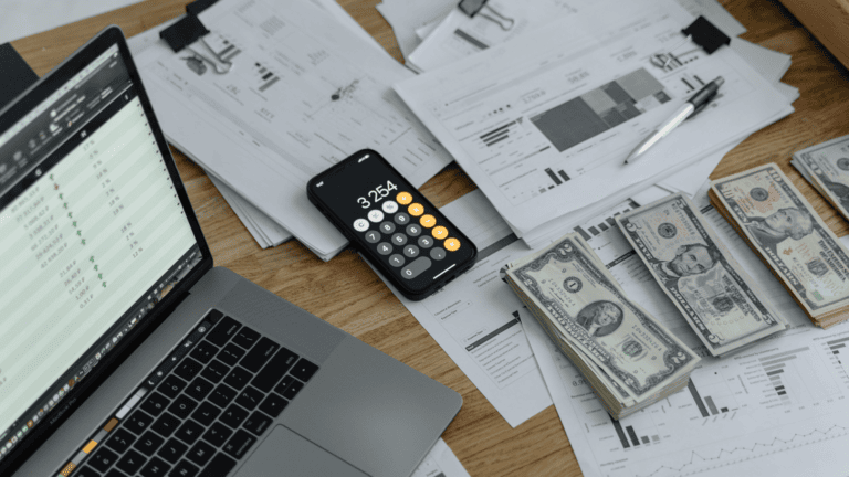 A computer, calculator and stacks of money on a desk