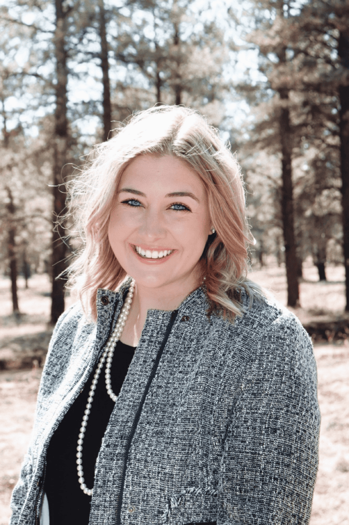 A smiling woman standing in front of a line of trees