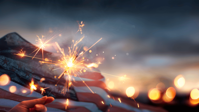 Person holding sparkler over US flag for July 4th celebration