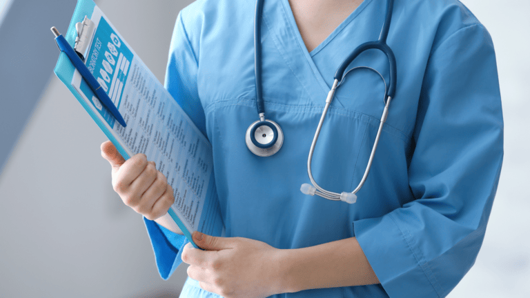 A person wearing scrubs and a stethoscope holds a clip board