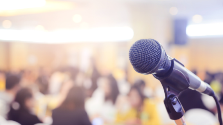 Microphone in focus with a blurred audience in the background.